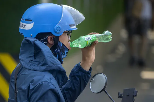 A delivery driver takes a drink as he waits at a traffic light on an unseasonably hot day in Beijing, Saturday, June 24, 2023. (Photo by Mark Schiefelbein/AP Photo)