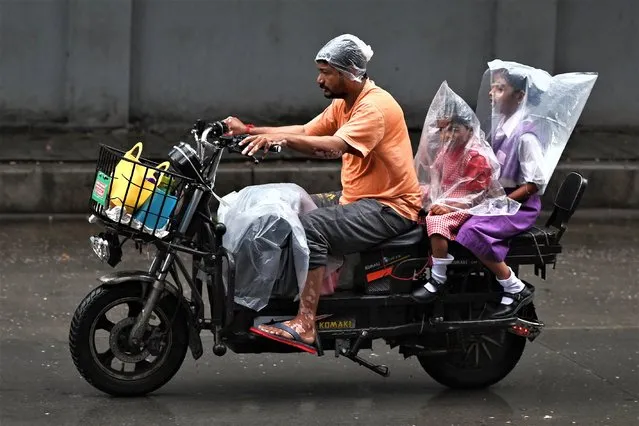 A man rides a two-wheeler with two children covered with plastic sheets during a monsoon rainfall in Hyderabad on July 18, 2023. (Photo by Noah Seelam/AFP Photo)