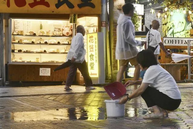 A person scoops out water from an arcade in Naha, Okinawa prefecture, southern Japan Sunday, August 6, 2023. A meandering storm was headed again toward southwestern Japan on Sunday, prompting fresh warnings about dangerously heavy rainfall after the same area was hit several days ago. (Photo by Kyodo News via AP Photo)