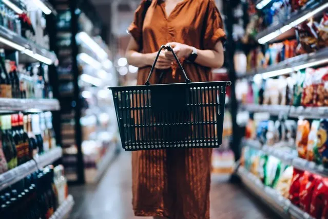 Cropped shot of young woman carrying a shopping basket, standing along the product aisle, grocery shopping for daily necessities in supermarket. (Photo by d3sign/Getty Images)