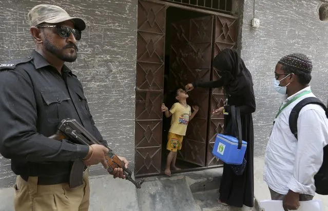 A police officer stands guard while a healthcare worker administers a polio vaccine to a child, in Karachi, Pakistan, Wednesday, June 9, 2021. Gunmen on a motorcycle Wednesday shot and killed two police officers assigned to protect polio vaccination workers in the district of Mardan in Khyber Pakhtunkhwa province, northwest Pakistan before fleeing, police said. (Photo by Fareed Khan/AP Photo)