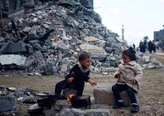 Palestinian children sit by the fire next to the rubble of a house hit in an Israeli strike during the conflict, amid a temporary truce between Hamas and Israel, in Khan Younis in the southern Gaza Strip on November 27, 2023. (Photo by Mohammed Salem/Reuters)