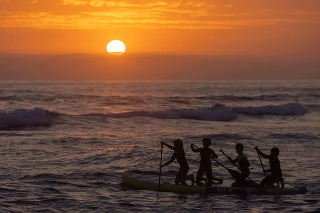 A group of kids paddle out into the waves as the sun sets at Cardiff State Beach in California, U.S. July 8, 2021. (Photo by Mike Blake/Reuters)