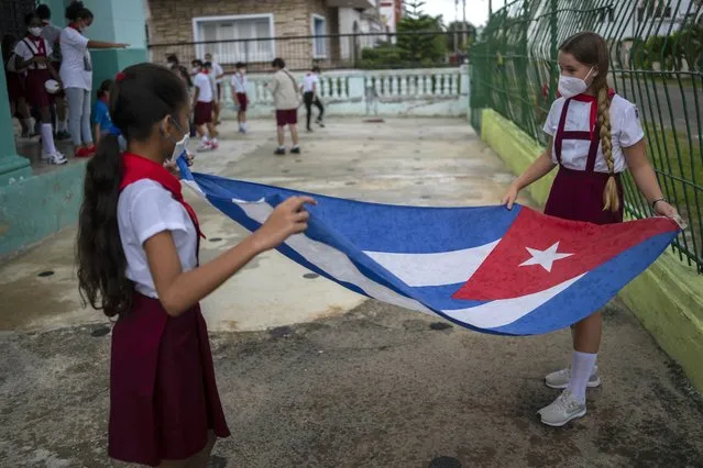 Students wearing masks as a precaution amid the spread of COVID-19 put away a Cuban flag so it does not get wet in the rain on their first day of school after months without face-to-face classes in Havana, Cuba, Monday, November 8, 2021. As Cuba approaches the announced date of Nov. 15 for the reopening of the entire country to the world, getting children back to school is one of its priorities. (Photo by Ramon Espinosa/AP Photo)