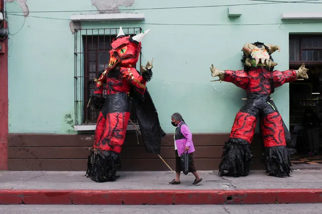 A woman walks past 3 meters tall pinatas shaped like the devil during the annual celebration of the “Burning of the Devil”, a festivity associated with the Feast of the Immaculate Conception which honors the city's patron saint, in Guatemala City, Guatemala December 7, 2021. (Photo by Sandra Sebastian/Reuters)