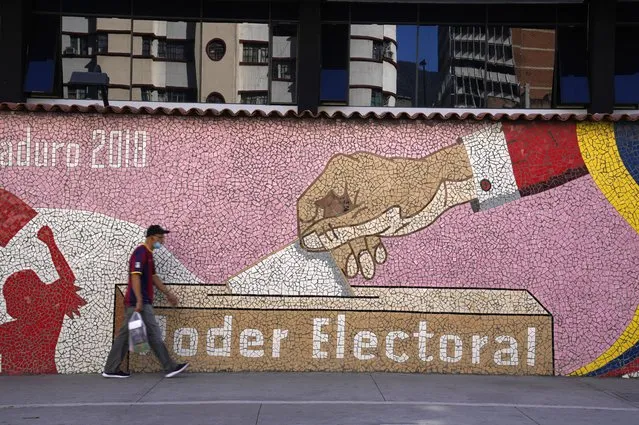 A man walks past a mural with an image of a ballot being cast and the words in Spanish “Electoral Power”, in Caracas, Venezuela, Tuesday, November 30, 2021. Venezuela's Supreme Court ordered a repeat election for the governorship of Barinas, the home state of the late President Hugo Chávez, excluding the opposition candidate Adolfo Superlano, who was emerging as the winner of the Nov. 21, regional election. (Photo by Ariana Cubillos/AP Photo)