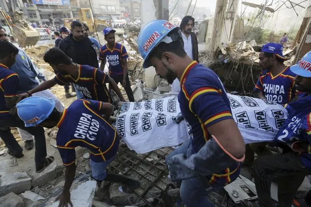 Rescue people carry the dead body of a victim after a gas explosion in Karachi, Pakistan, Saturday, December 18, 2021. Officials said the powerful gas explosion in a sewage system in the southern Pakistan city has killed multiple people and injured others. (Photo by Fareed Khan/AP Photo)