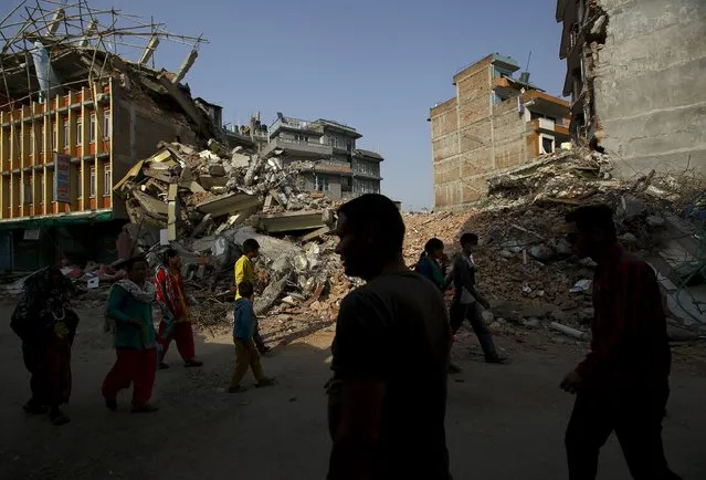 Nepalese people walk along a street near the debris of collapsed houses, a month after the April 25 earthquake in Kathmandu, Nepal May 25, 2015. (Photo by Navesh Chitrakar/Reuters)
