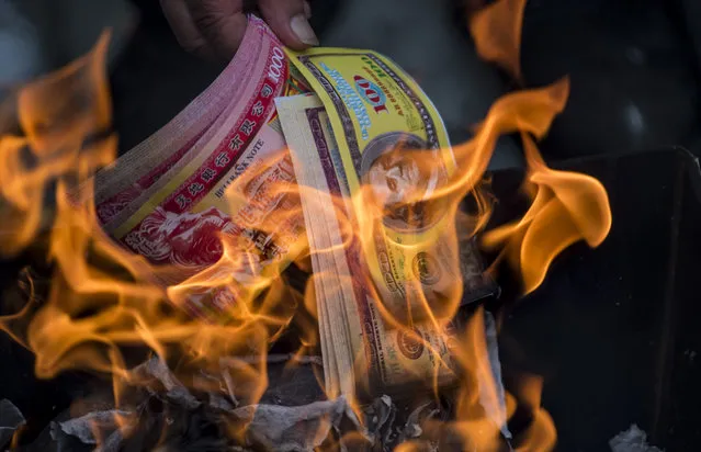 A man burns ghost money to pay his respects to his ancestors in front of a gravestone during the annual “Qingming” festival, or Tomb Sweeping Day, at a public cemetery in Shanghai on April 4, 2017. During Qingming, Chinese traditionally tend the graves of their departed loved ones and often burn paper money, model houses, cars, mobile phones and other goods as offerings to honour them and keep them comfortable in the afterlife. (Photo by Johannes Eisele/AFP Photo)