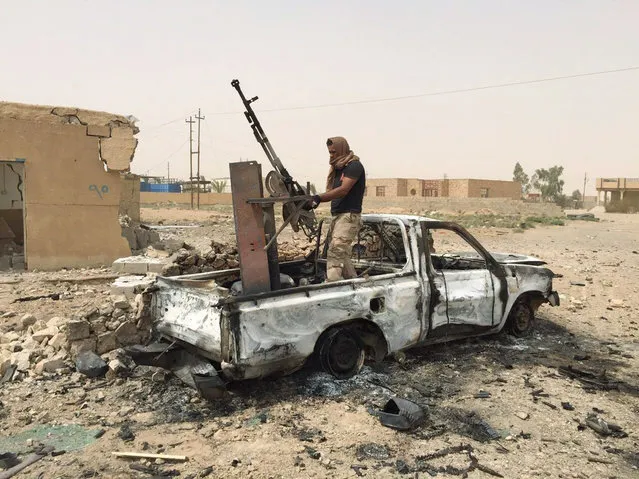 A militiaman allied with the Iraqi security forces dismantles a weapon from a destroyed vehicle belonging to the Islamic State group following a U.S.-led coalition airstrike against IS positions in southern Ramadi, Anbar province, Iraq, Monday, July 20, 2015. Iraqi security officials said that militants from the Islamic State group blew up a sports stadium near the militant-held city of Ramadi. (Photo by AP Photo)