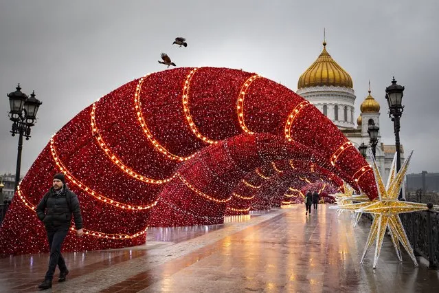 People walk on the Patriarch's bridge decorated for Christmas and New Year celebrations with the Christ the Savior Cathedral in the background in Moscow, Russia, Monday, December 16, 2019. (Photo by Alexander Zemlianichenko/AP Photo)