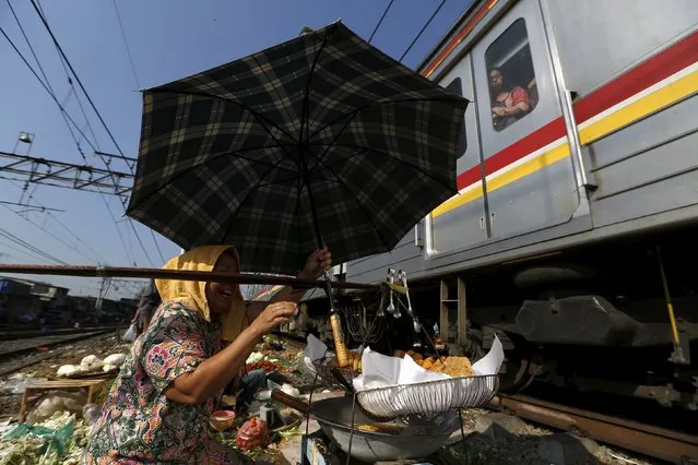 A woman holds her umbrella while selling food as a train passes through a vegetable market located on train tracks near Duri train station in Jakarta, Indonesia August 3, 2015. (Photo by Reuters/Beawiharta)