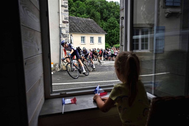 A little girl looks out a window as the pack of riders cycles past during the 5th stage of the 110th edition of the Tour de France cycling race, 163 km between Pau and Laruns, in the Pyrenees mountains in southwestern France, on July 5, 2023. (Photo by Marco Bertorello/AFP Photo)