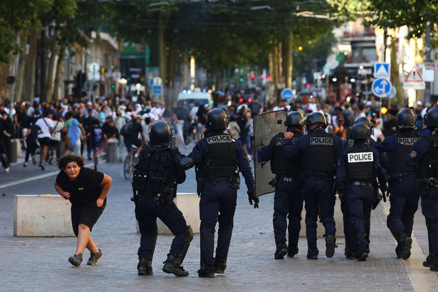 A girl ducks down as she walks past police officers preparing to disperse protesters with tear gas during a demonstration against police in Marseille, southern France on July 1, 2023, after a fourth consecutive night of rioting in France over the killing of a teenager by police. French police arrested 1311 people nationwide during a fourth consecutive night of rioting over the killing of a teenager by police, the interior ministry said on July 1, 2023. France had deployed 45,000 officers overnight backed by light armoured vehicles and crack police units to quell the violence over the death of 17-year-old Nahel, killed during a traffic stop in a Paris suburb on July 27, 2023. (Photo by Clement Mahoudeau/AFP Photo)