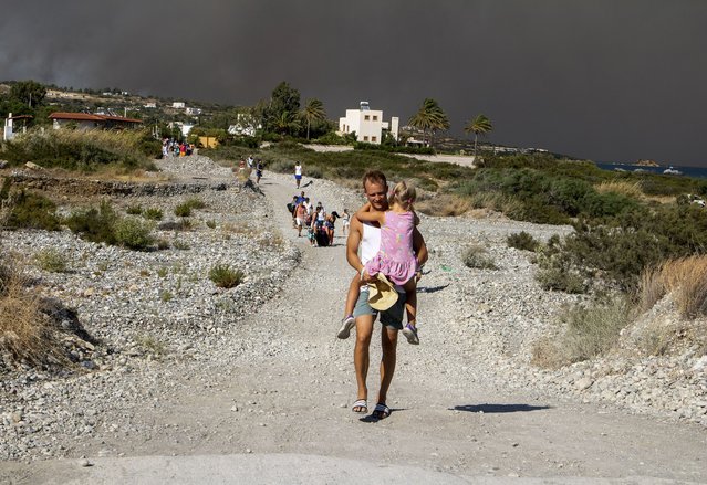 A man carries a child as they leave an area where a forest fire burns, on the island of Rhodes, Greece, Saturday, July 22, 2023. A large wildfire burning on the Greek island of Rhodes for a fifth day has forced authorities to order an evacuation of four locations, including two seaside resorts. Photo by (Lefteris Diamanidis/InTime News via AP Photo)