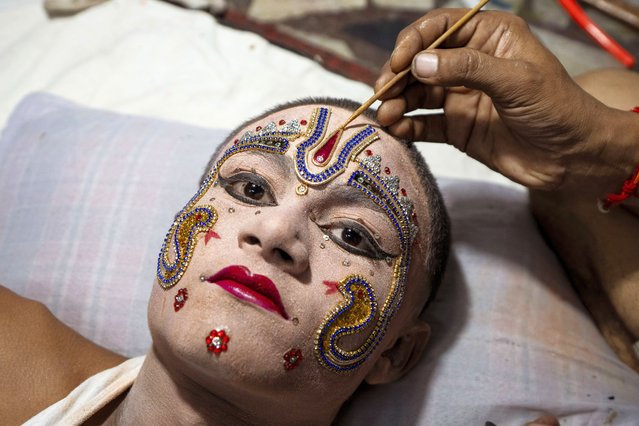 An Indian man applies makeup on artist Krishna Shukla, 14, dressed up as Hindu God Laxman, ahead of a religious procession during the Dussehra festival, also known as Vijayadashami, the day Rama killed demon King Ravana who had abducted Rama's wife Sita, celebrating the victory of good over evil every the 12th of October, in Prayagraj in the northern Indian state of Uttar Pradesh, India, Wednesday, October 9, 2024. (Photo by Rajesh Kumar Singh/AP Photo)