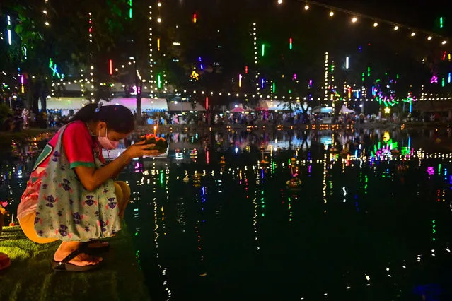 A woman sets a krathong into the water in Bangkok in November 19, 2021 during Loy Krathong, an annual festival in which floating decorative rafts are released into rivers and ponds across the country during the evening of the full moon of the 12th Thai lunar month. (Photo by Lillian Suwanrumpha/AFP Photo)