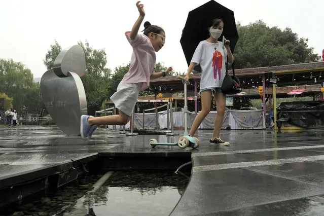 A child leaps across a water feature during a rainy day in Beijing, Sunday, August 14, 2022. (Photo by Ng Han Guan/AP Photo)