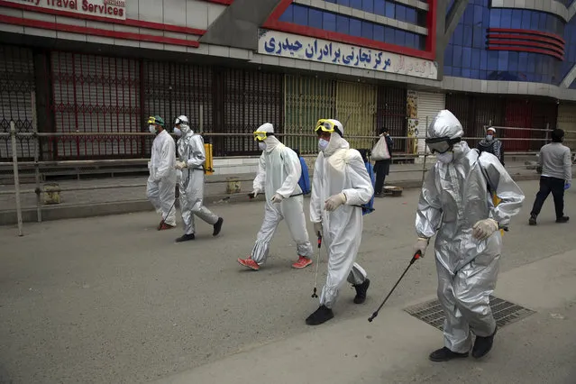 Volunteers in protective suits spray disinfectant on storefronts to help curb the spread of the coronavirus in Kabul, Afghanistan, Sunday, March 29, 2020. The government Friday ordered a three-week lock-down for Kabul to stem the spread of the new coronavirus. (Photo by Rahmat Gul/AP Photo)