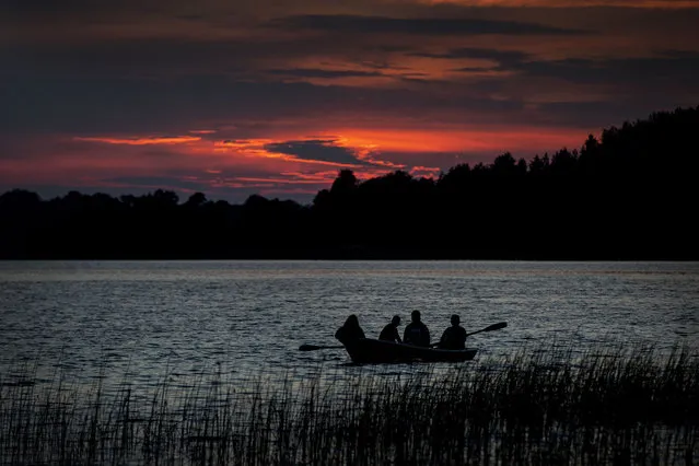 People row on a boat during sunset on the lake near the small town of Ignalina, some 120km (74.5 miles) north of the capital Vilnius, Lithuania, Saturday, July 23, 2022. (Photo by Mindaugas Kulbis/AP Photo)