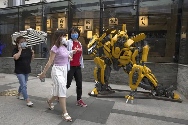 Residents wearing face masks to curb the spread of the coronavirus walk past a sculpture depicting a character from the Transformer movie outside a restaurant in Beijing on Monday, June 8, 2020. A semblance of normalcy has returned to the Chinese capital as businesses open and residents go about their usual activities. (Photo by Ng Han Guan/AP Photo)