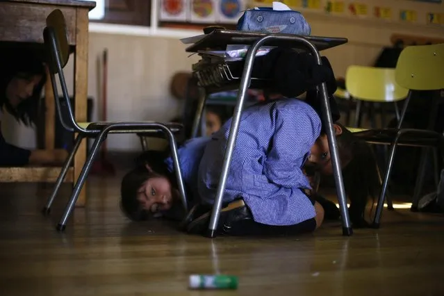 Children take cover under their desk inside a school during an earthquake drill in Santiago, November 13, 2014. (Photo by Ivan Alvarado/Reuters)