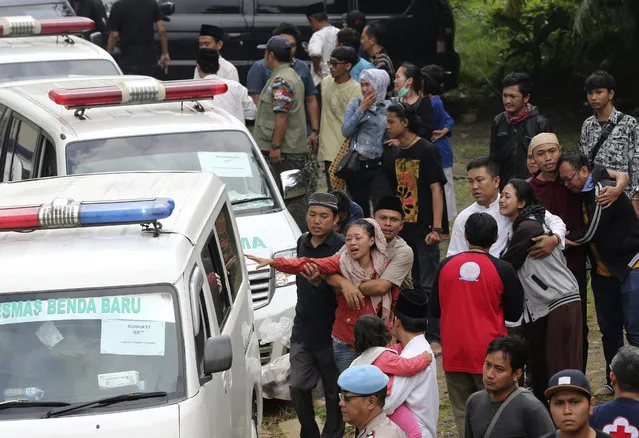 Relatives react as ambulances carrying the bodies of the victims of a bus accident arrive at their home village in East Ciputat, Indonesia, Sunday, February 11, 2018. A packed tourist bus returning from an outing collided with a motorbike and plunged from a hill on Indonesia's main island of Java after its brakes apparently malfunctioned. (Photo by Tatan Syuflana/AP Photo)