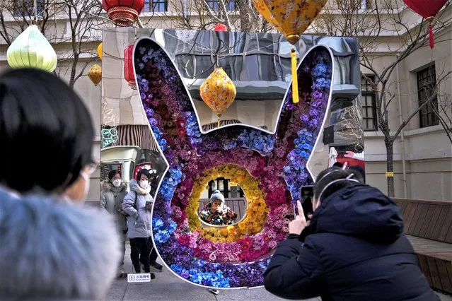 Women wearing face masks watch a toddler pose for a souvenir photo with a rabbit shaped floral decoration at a pedestrian shopping street at Qianmen on the first day of the Lunar New Year holiday in Beijing, Sunday, January 22, 2023. People across China rang in the Lunar New Year on Sunday with large family gatherings and crowds visiting temples after the government lifted its strict “zero-COVID” policy, marking the biggest festive celebration since the pandemic began three years ago. (Photo by Andy Wong/AP Photo)