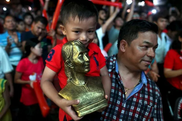 A boy carries a bust depecting Myanmar's pro-democracy leader Aung San Suu Kyi while gathering to see partial results shown on a TV outside NLD party headquarters in Yangon, November 8, 2015. (Photo by Soe Zeya Tun/Reuters)