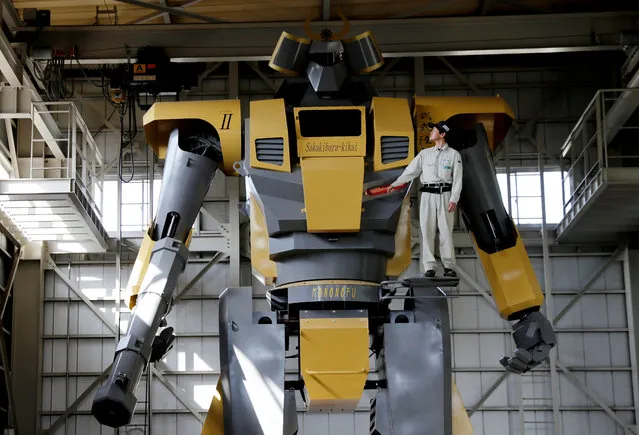 Sakakibara Kikai's engineer Go Sakakibara poses with the bipedal robot Mononofu during its demonstration at its factory in Shinto Village, Gunma Prefecture, Japan on April 12, 2018. Developed at Sakakibara Kikai, a maker of farming machinery, LW-Mononofu is a 28-feet tall, two-legged robot weighing in at more than 7 tonnes. It contains a cockpit with monitors and levers for the pilot to control the robot's arms and legs. (Photo by Kim Kyung-Hoon/Reuters)