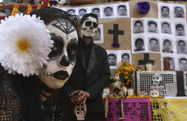 A “catrina” and “calavera” stand in front of a Day of the Dead altar honoring the 43 disappeared rural college students in Acapulco, Mexico, Wednesday, October 26, 2016. The government's initial investigation decided the students were killed and incinerated in a fire in 2014. But international experts have cast doubt on this theory and the families have not accepted it. (Photo by Bernandino Hernandez/AP Photo)