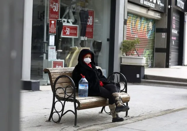 A woman wearing a mask to help protect against the spread of coronavirus, rests in a deserted street after shopping for food during a two-day weekend curfew, in Ankara, Turkey, Sunday, January 24, 2021. Turkey has passed the milestone 25,000 COVID-19 deaths on Sunday. (Photo by Burhan Ozbilici/AP Photo)