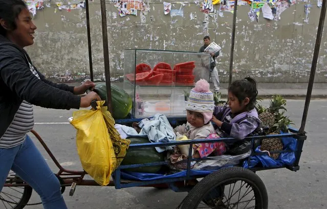 A woman sells fruits while children sit in a tricycle cart in downtown Lima, Peru December 1, 2015. (Photo by Mariana Bazo/Reuters)