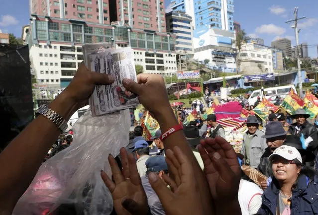 People reach for imitation bank notes that were blessed by a witch doctor during the “Alasitas” fair in La Paz January 24, 2015. (Photo by David Mercado/Reuters)