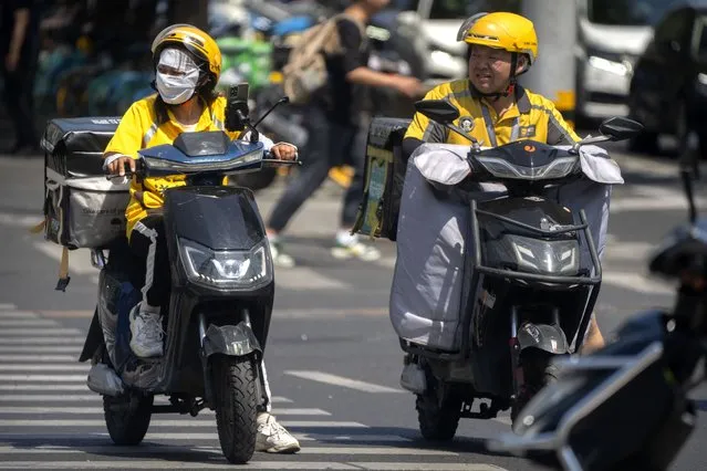 A delivery driver wears a face covering to protect themselves from the sun as they wait at an intersection on an unseasonably hot day in Beijing, Saturday, June 24, 2023. (Photo by Mark Schiefelbein/AP Photo)