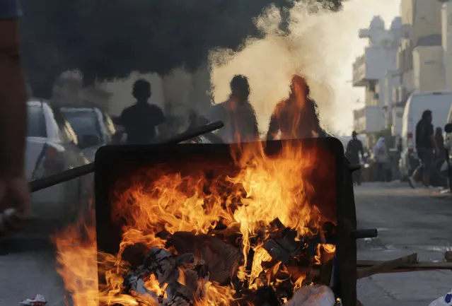 Bahraini anti-government protesters stand near a burning garbage dumpster, using the fire to ease the tear gas in the air, during clashes with riot police in Sitra, Bahrain, Friday, January 1, 2016. February 14 – the most active street opposition network in Bahrain – called a New Year's Day demonstration to give a fresh push to its nearly 5-year-old fight against Bahrain's monarchy. (Photo by Hasan Jamali/AP Photo)