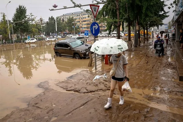 A woman walks on a muddy street next to damaged by flood cars during a downpour in Mentougou District, west of Beijing, China on August 1, 2023. Heavy rains brought by Typhoon Doksuri caused floods in northern China and left two dead and thousands being evacuated as Beijing experienced its heaviest rainfall of the year. (Photo by Mark R. Cristino/EPA/EFE)