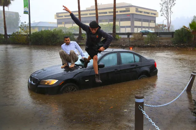 Octavio Angulo jumps as Mike Patel, left, looks on as the two abandon their vehicle after a flooded road stalled their vehicles engine in San Diego, Calif. El Nino storms lined up in the Pacific, promising to drench parts of the West for more than two weeks and increasing fears of mudslides and flash floods in regions stripped bare by wildfires. (Photo by Nelvin C. Cepeda/The San Diego Union-Tribune via AP Photo)