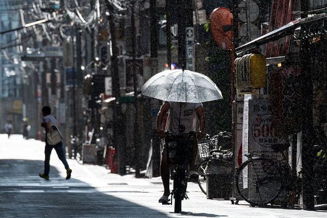 A man rides his bicycle as it sprinkles with rain along a street outside Asakusabashi station in the Taito district of Tokyo on August 6, 2023. (Photo by Richard A. Brooks/AFP Photo)