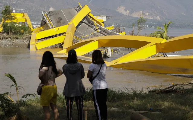 In this October 4, 2018, photo, villagers look at the damage on the city's iconic yellow Teluk Palu Bridge after a massive earthquake and tsunami damaged their seaside village in Palu, Central Sulawesi, Indonesia. The family lost their son. The 7.5 magnitude quake triggered not just a tsunami that leveled huge swathes of the region's coast, but a geological phenomenon known as liquefaction, making the soil move like liquid and swallowing entire neighborhoods. (Photo by Aaron Favila/AP Photo)