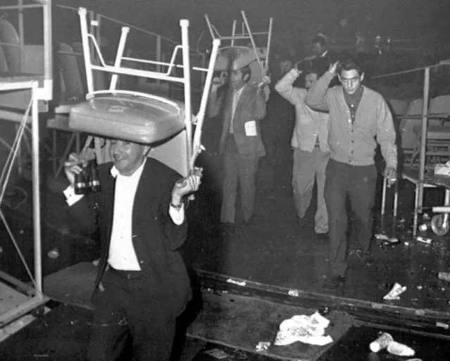 Fans use chairs to protect their heads as they flee from the Forum in Los Angeles, USA, December 7, 1968, after a riot broke out following the fight between Lionel Rose of Australia and Chucho Castillo of Mexico. Castillo's fans were angry over the result of a split decision in favor of Rose and created havoc in the arena. (Photo by AP Photo)