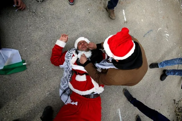 A man tends to a Palestinian protester, dressed as Santa Claus, after inhaling tear gas fired by Israeli troops during clashes in the West Bank city of Bethlehem, December 23, 2016. (Photo by Mussa Qawasma/Reuters)