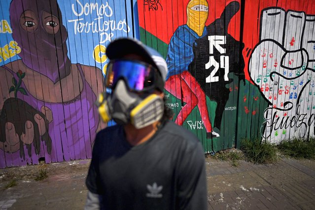 A demonstrator stands next to murals relates to protests against the government of Colombian President Ivan Duque in Cali, Colombia on June 3, 2021. (Photo by Luis Robayo/AFP Photo)