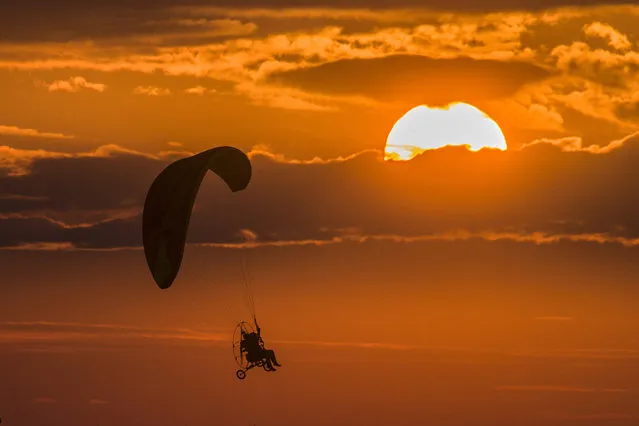 A man pilots a motorised hang glider at sunset in Ivanovo Region, Russia on July 17, 2021. (Photo by Vladimir Smirnov/TASS)