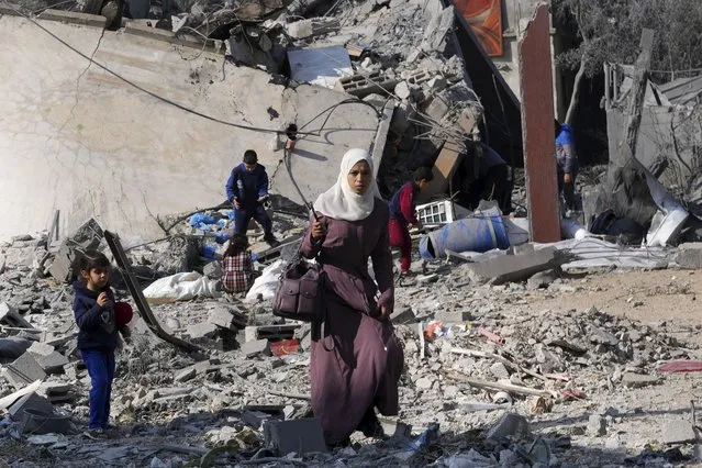 Palestinians walk by the rubble of a building of the Hamad family destroyed in an Israeli strike in Deir al Balah, Gaza Strip, Friday, December 29, 2023. (Photo by Adel Hana/AP Photo)