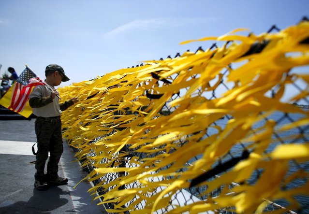 A young Vietnamese boy looks at some of the 58,300 yellow ribbons tied to a fence surrounding the flight deck of the USS Midway as the ship commemorates the 40th Anniversary of Operation Frequent Wind and the fall of Saigon in San Diego, California, United States April 26, 2015. (Photo by Mike Blake/Reuters)