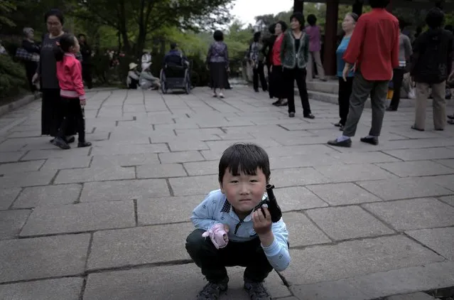 A North Korean boy plays with a toy pistol as elderly people gather around a gazebo, Sunday, May 3, 2015, at the Moranbong, or Moran Hill, in Pyongyang, North Korea. (Photo by Wong Maye-E/AP Photo)