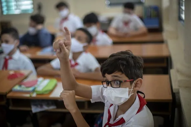 A student wearing a mask as a precaution amid the spread of COVID-19 raises his hand on the first day of school after months without face-to-face classes in Havana, Cuba, Monday, November 8, 2021. (Photo by Ramon Espinosa/AP Photo)