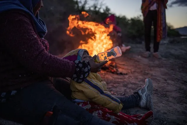 Alejandra, 32, feeds her one-year-old nephew Manuel as they sit near a fire to stay warm during cold and blustery weather while searching for an entry point into the United States from along the bank of the Rio Grande River in El Paso, Texas, U.S., April 1, 2024. (Photo by Adrees Latif/Reuters)