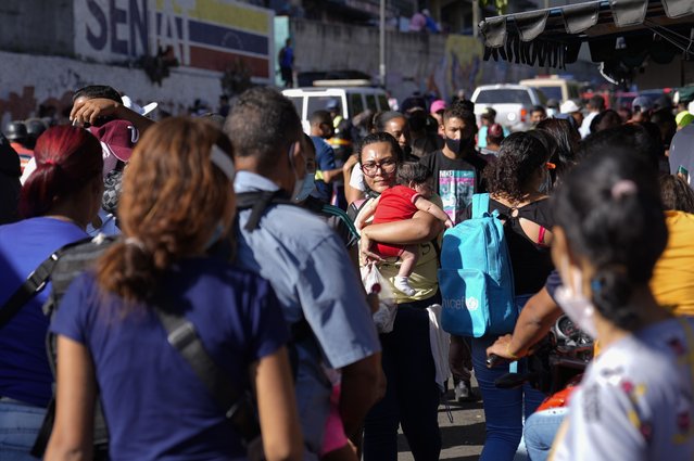 A woman walks with a baby in her arms on a crowed street in Caracas, Venezuela, Tuesday, November 30, 2021. (Photo by Ariana Cubillos/AP Photo)
